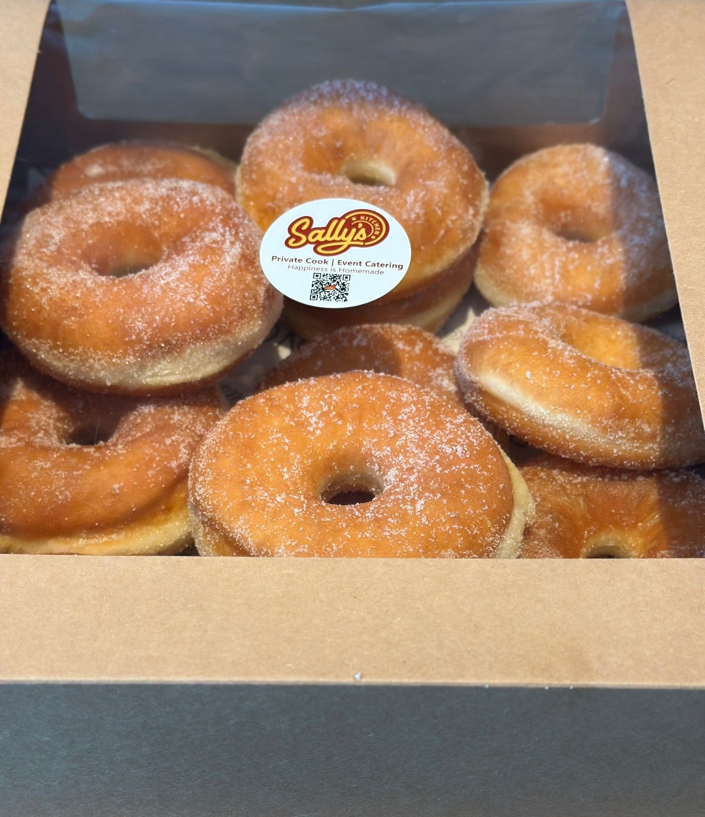 Box of sugared donuts with a Sally's Donuts label on a wooden surface