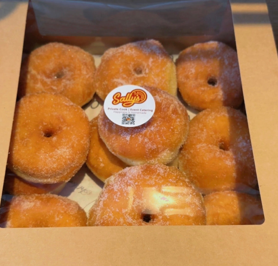 Box of sugared donuts with Sallys kitchen label on a wooden surface