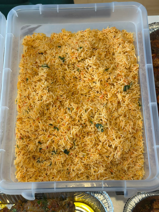 Container of yellow coconut rice with green herbs on a wooden surface