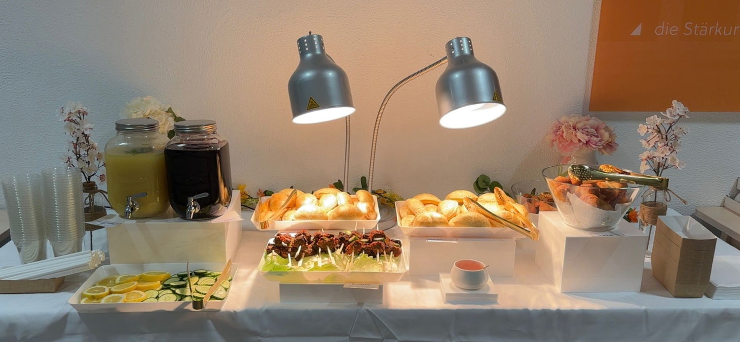 Buffet table with various food items under two silver lamps.