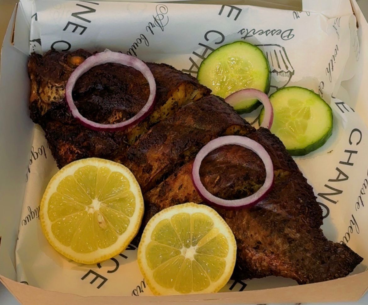 Grilled fish with lemon slices, onions, and cucumbers on a branded paper
