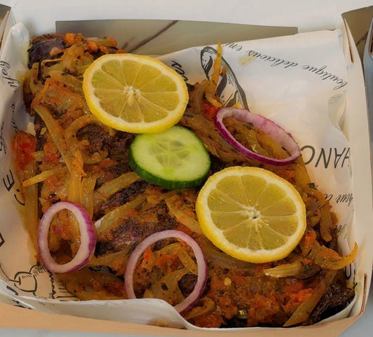 Plated dish of peppered tilapia with lemon slices, cucumber, and onions on a branded paper liner.