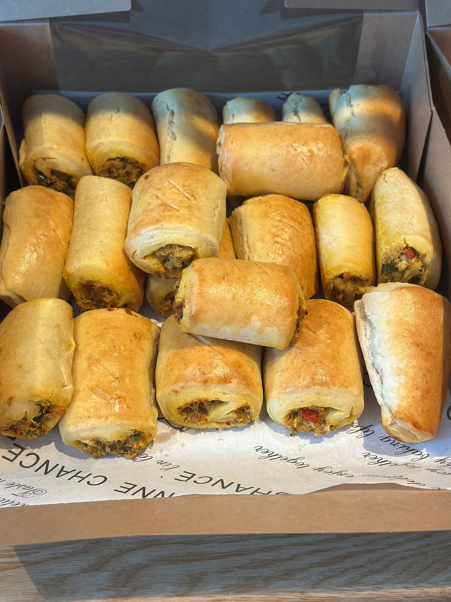 Box of golden-brown fish rolls on a cardboard surface