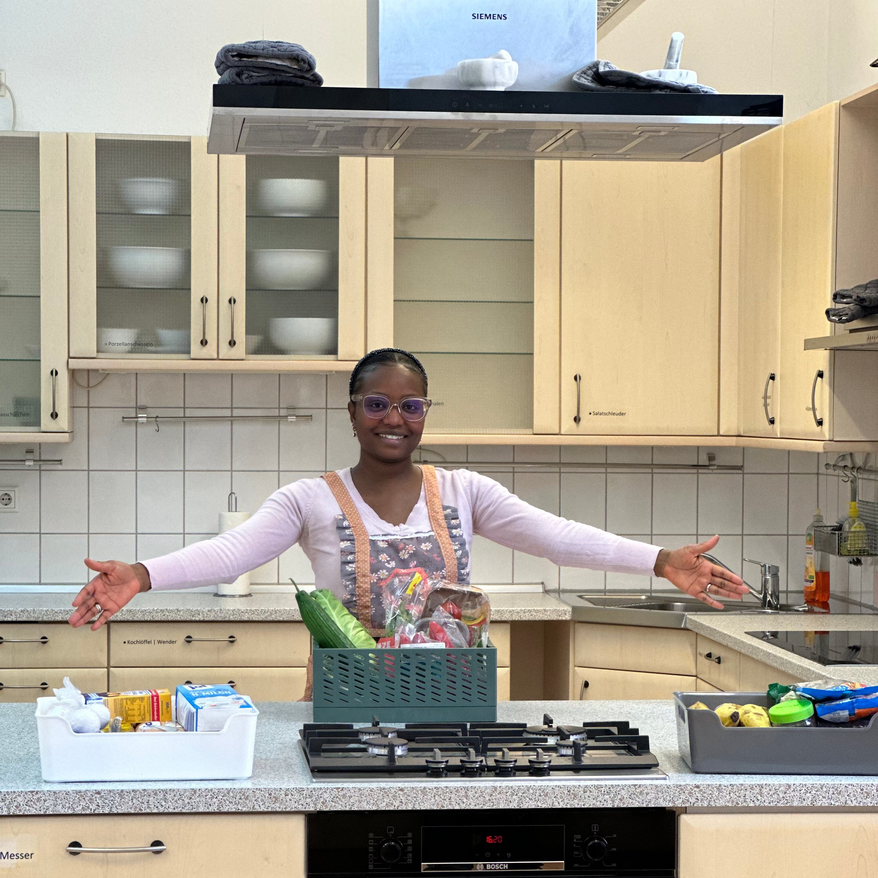 Woman in a kitchen with cabinets, appliances, and various items on the counter.